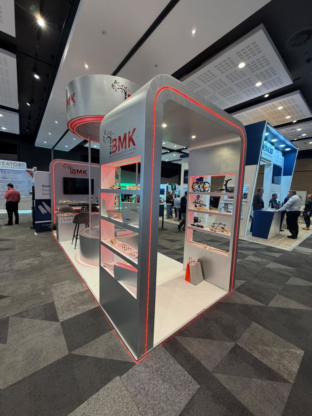 Custom exhibition stand built for BMK Orthopaedics, showing the shelved product display side with illuminated red trim