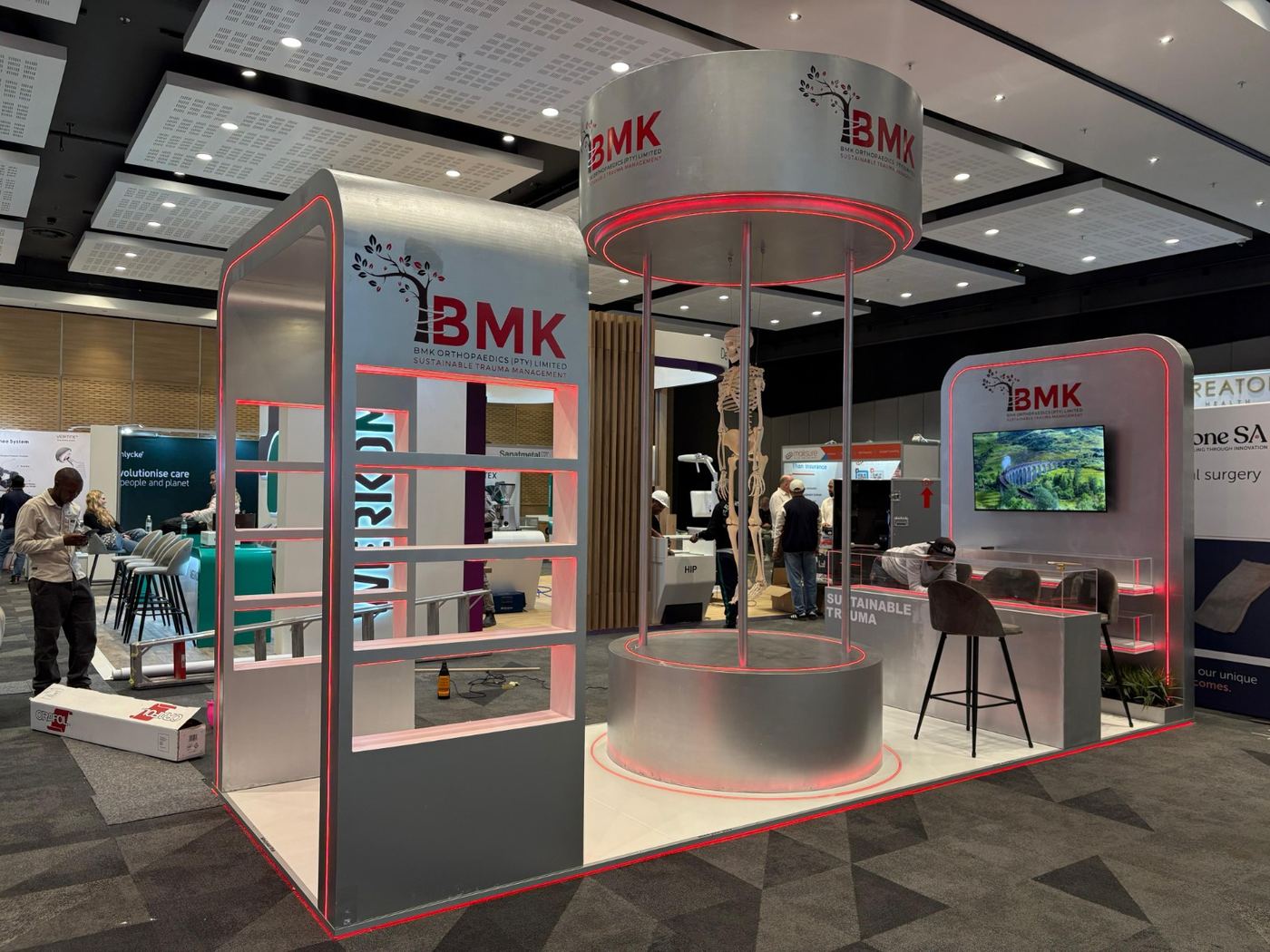 Custom exhibition stand built for BMK Orthopaedics, with a cylindrical entrance tower, illuminated red trim and a lounge seating area