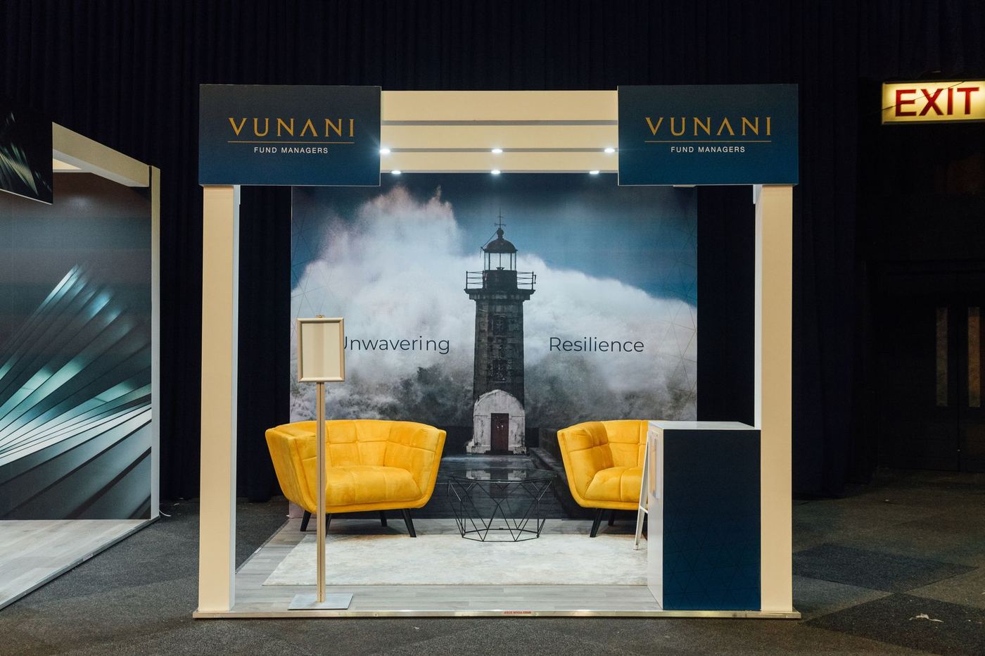 Custom exhibition stand built for Vunani Fund Managers, featuring a lighthouse feature wall with an 'Unwavering, Resilience' theme and lounge seating