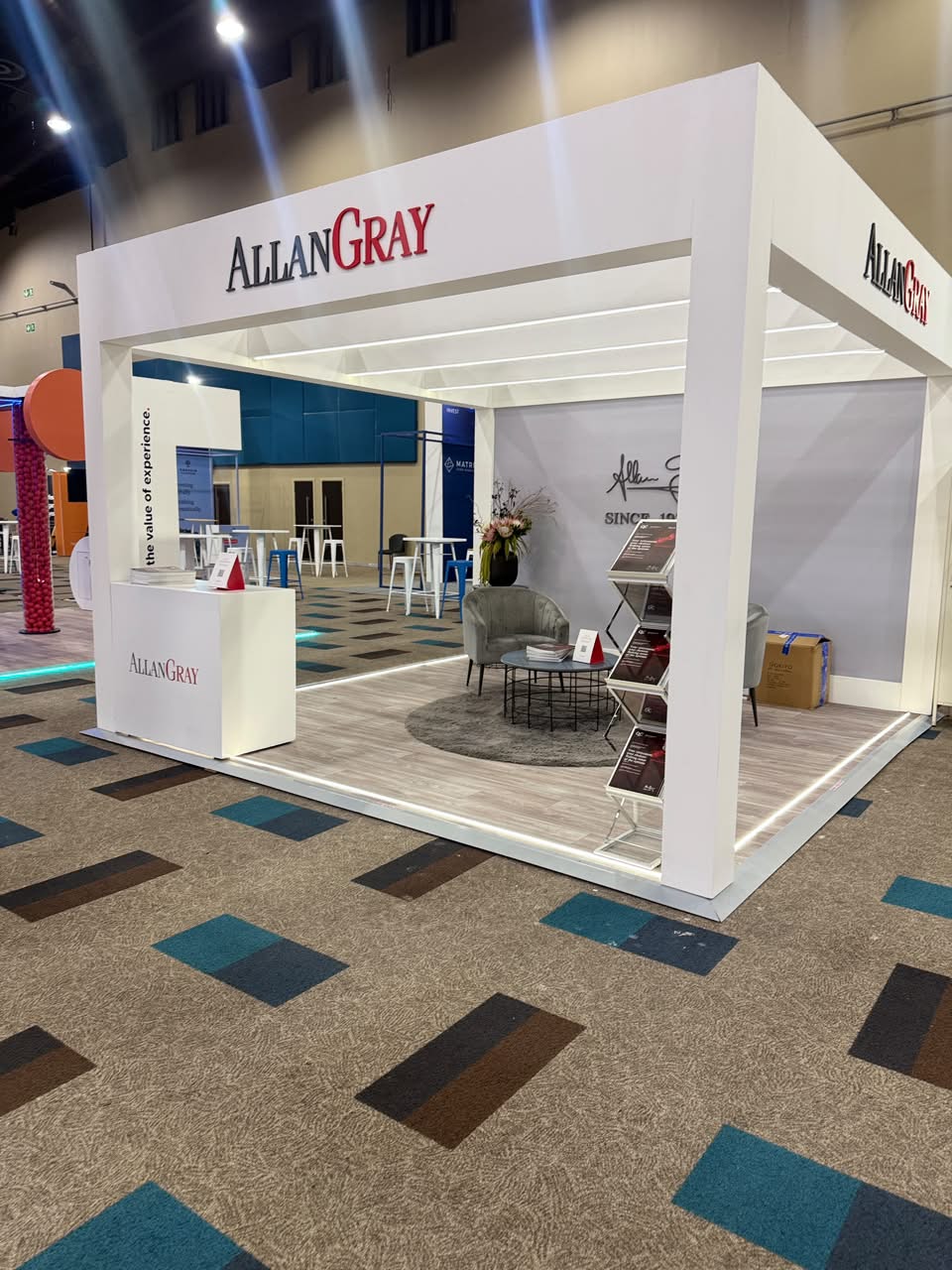 Custom exhibition stand built for Allan Gray, with branded pergola framing, a lounge seating area and a literature display