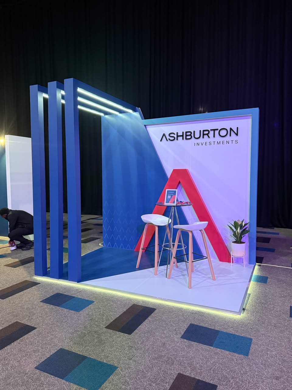 Custom exhibition stand built for Ashburton Investments, with a bold red 'A' backdrop and blue fin-panel framing