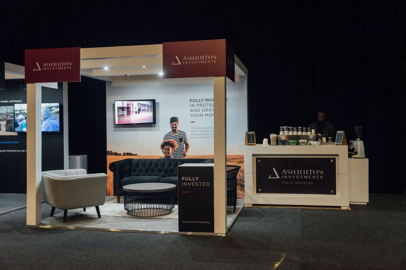 Custom exhibition stand built for Ashburton Investments, with an archway entrance and branded coffee bar