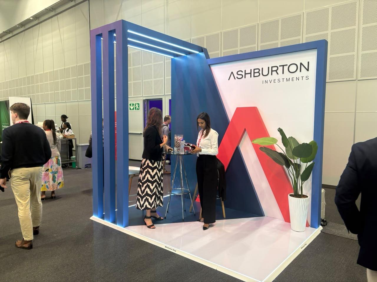 Custom exhibition stand built for Ashburton Investments, shown live with visitors at the bold red 'A' backdrop