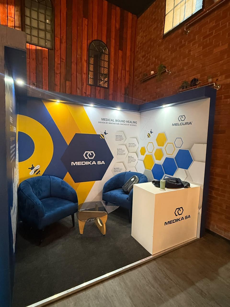 Custom exhibition stand built for Medika SA, with a yellow and navy hexagon-patterned feature wall and 'Medical Wound Healing' messaging
