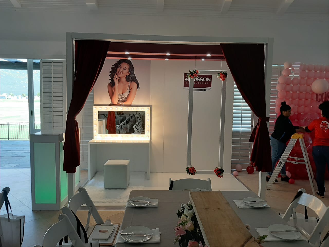 Styled event furniture and dining setup with a branded backdrop and balloon display