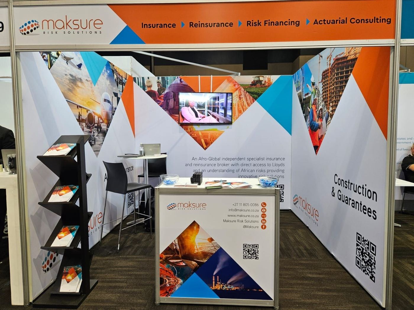 Shell scheme exhibition stand built for Maksure Risk Solutions, with full-height graphic panelling, a literature stand and a branded reception counter