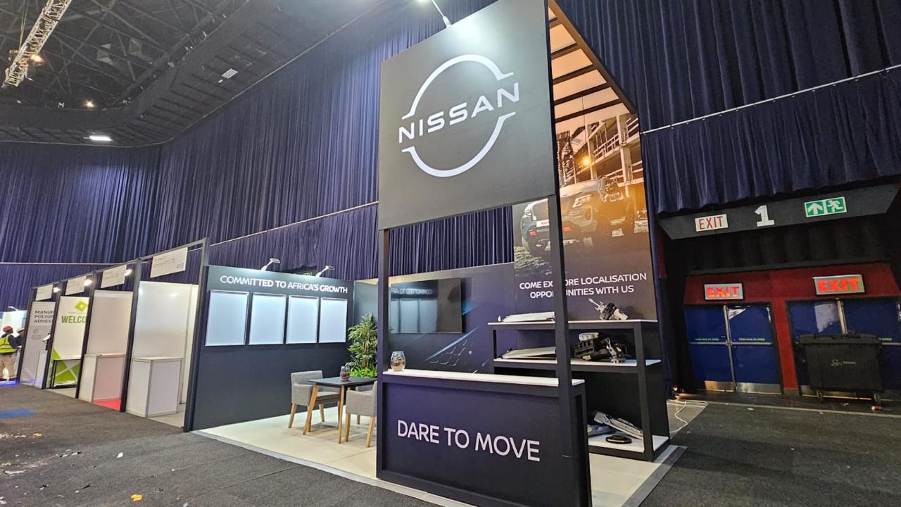 Shell scheme exhibition stand built for Nissan, with a tall illuminated sign, seating area and 'Dare to Move' branded messaging