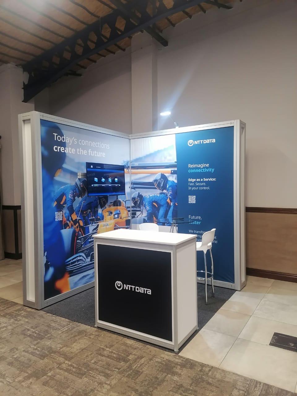 Shell scheme exhibition stand built for NTT DATA, with full-height graphic panelling and a branded reception counter
